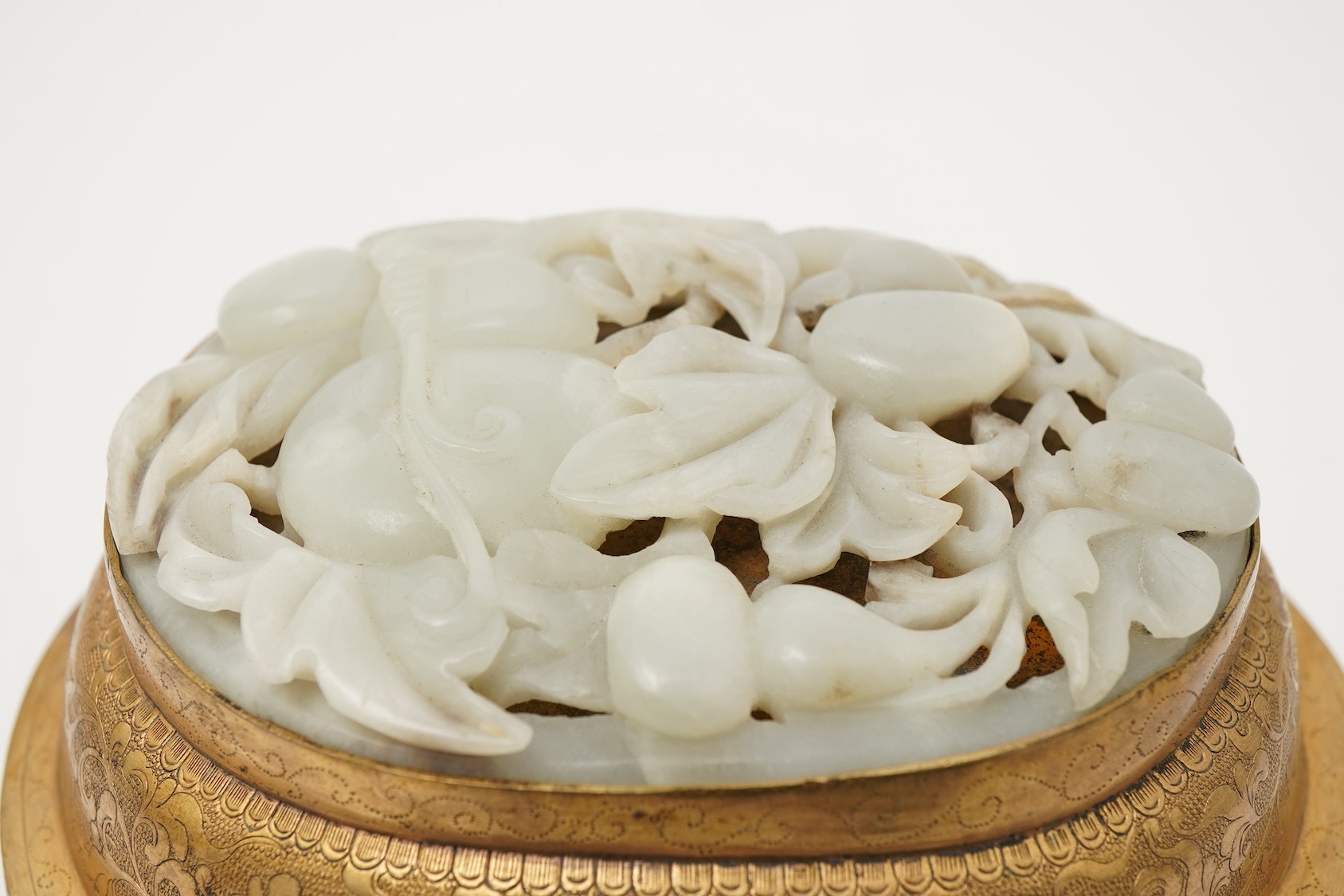 A Chinese pale celadon jade oval plaque, 17th/18th century, mounted on a late Qing gilt copper jar
